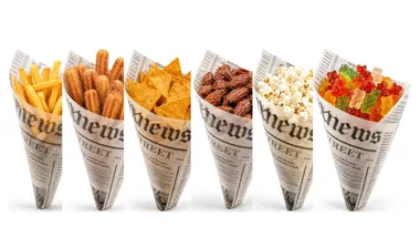 Sechs gefüllte Papiertüten im Zeitungsdruck-Motiv nebeneinander auf einer Linie: Pommes frites, Churros, Nachos, gebrannte Mandeln, Popcorn und Gummibärchen.